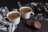 Two white ceramic mugs filled with hot chocolate, each with a spoon, next to two chocolate cookies and a checkered scarf.