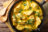 A cast iron pan filled with chicken curry and garnished with fresh parsley, with wooden spoons on the side.