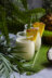 Two glasses of creamy white smoothie topped with pineapple wedges and garnished with a salt rim, placed on a banana leaf with a coconut and pineapple in the background.