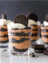 A chocolate and cream dessert in a glass jar, layered with crushed Oreos, topped with whipped cream and an Oreo cookie.