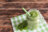 A green smoothie in a mason jar with a straw and mint leaves on a checkered napkin.