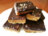 A pile of chocolate caramel bars with a crumbly base and sprinkled with nuts on a white plate