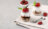 Two glass jars filled with yogurt parfaits layered with granola and chocolate sauce, topped with strawberries and mint.