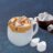 A mug of hot chocolate topped with marshmallows, chocolate drizzle, and graham cracker crumbs, with a bowl of marshmallows nearby.