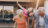 A multi-generational family laughing and playing outdoors, with a grandmother giving piggyback rides to grandchildren.